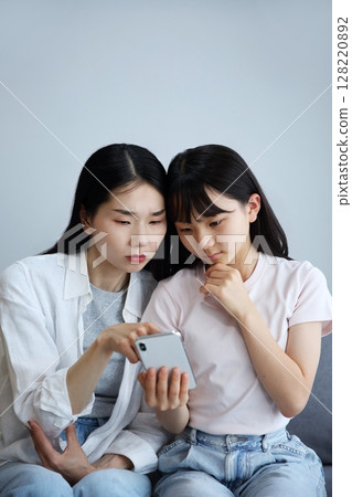 一位母親和女兒認真地看著智慧型手機的圖片 一位母親和女兒認真地看著智慧型手機的圖片 128220892