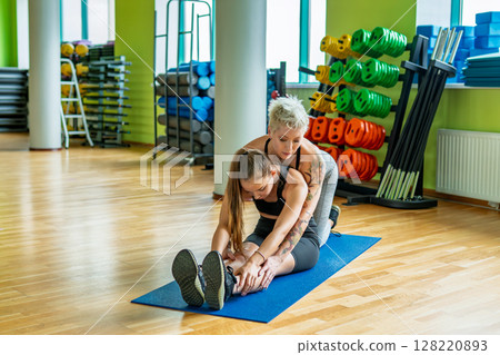 An Experienced Personal Trainer Providing Assistance During a Stretching Session in the Gym An Experienced Personal Trainer Providing Assistance During a Stretching Session in the Gym 128220893