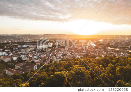 Golden sunlight illuminates Prague Castle and the historic city below at sunrise. The tranquil atmosphere sets the scene for a new day in this beautiful city filled with ancient architecture. 128220968