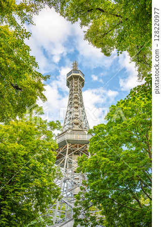 Petrin Lookout Tower rises above lush greenery under a cloudy sky in Prague. Visitors can enjoy stunning views from this iconic structure in the heart of the city. Petrin Lookout Tower rises above lush greenery under a cloudy sky in Prague. Visitors can enjoy stunning views from this iconic structure in the heart of the city. 128220977