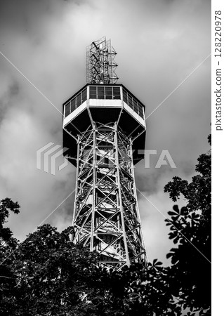 Petrin Lookout Tower rises prominently in Prague amidst a lush green setting. The structure's intricate design is highlighted against the cloudy backdrop, offering a glimpse of the city skyline. Petrin Lookout Tower rises prominently in Prague amidst a lush green setting. The structure's intricate design is highlighted against the cloudy backdrop, offering a glimpse of the city skyline. 128220978