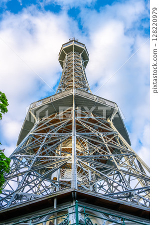 Tourists admire the Petrin Lookout Tower, a stunning landmark in Prague. The tower, resembling the Eiffel Tower, offers breathtaking views of the city against a backdrop of blue skies. Tourists admire the Petrin Lookout Tower, a stunning landmark in Prague. The tower, resembling the Eiffel Tower, offers breathtaking views of the city against a backdrop of blue skies. 128220979