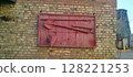 Vintage fire fighting tools displayed on a red wooden board, mounted on a brick wall. Axe, shovel, bucket, and hook. Fire shield. Displayed outdoors against a brick wall. Red wooden fire shield. 128221253