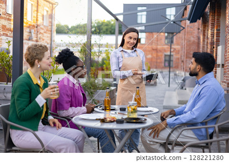 A female waiter presents a portable terminal to a customer, ready to process a payment at an outdoor cafe. A female waiter presents a portable terminal to a customer, ready to process a payment at an outdoor cafe. 128221280