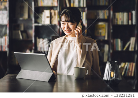 Asian woman using tablet PC while talking on the phone in study, library, businesswoman 128221281