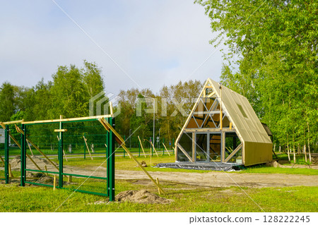 New A-Frame Glamping Cabin Under Construction in a Forested Campground with Green Fence Nearby 128222245