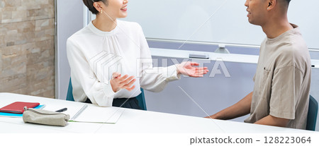 A black man and a Japanese woman having a conversation in a classroom 128223064