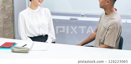 A black man and a Japanese woman having a conversation in a classroom 128223065