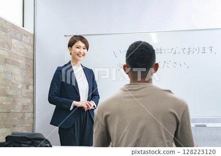A female teacher teaches business terms to a black man at a Japanese language school 128223120