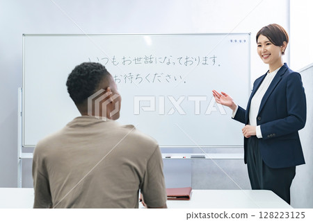 A female teacher teaches business terms to a black man at a Japanese language school A female teacher teaches business terms to a black man at a Japanese language school 128223125