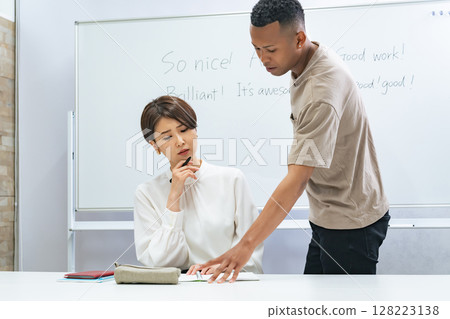 A black man and a Japanese woman having a conversation in a classroom 128223138