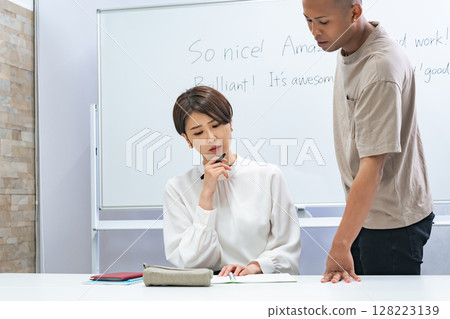 A black man and a Japanese woman having a conversation in a classroom 128223139