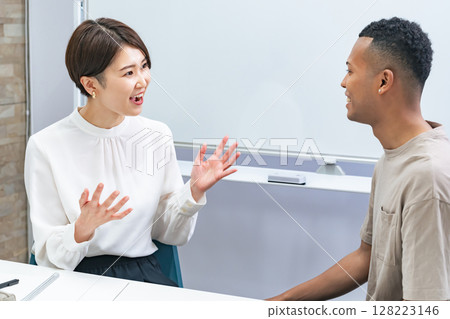 A black man and a Japanese woman having a conversation in a classroom 128223146