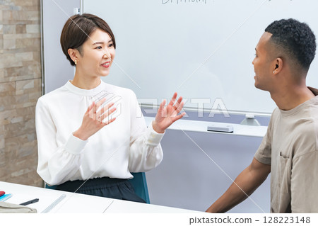 A black man and a Japanese woman having a conversation in a classroom 128223148