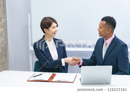A black male businessman and a Japanese female staff member shaking hands in front of a whiteboard 128223161
