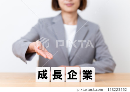 A middle-aged female business woman wearing a suit and a block of a growing company A middle-aged female business woman wearing a suit and a block of a growing company 128223362
