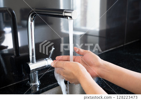 Hands of woman wash their hands in a sink with foam to wash the skin and water flows through the hands. Concept of health, cleaning and preventing germs and coronavirus from contacting hands 128223473