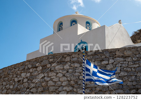 Greek flag waving in front of a traditional white and blue church in greece Greek flag waving in front of a traditional white and blue church in greece 128223752