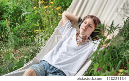 Teenage girl relaxing in hammock listening to music outdoors Teenage girl relaxing in hammock listening to music outdoors 128225184