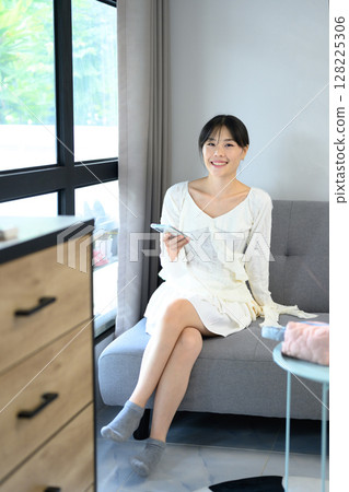 Pretty asian woman using smartphone on a sofa at home in a bright living room 128225306