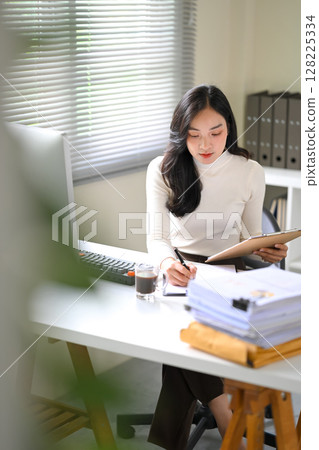 Focused businesswoman reviewing documents at her desk in a modern office 128225334