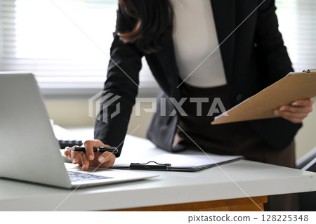 Businesswoman analyzing financial data with clipboard and laptop on office desk Businesswoman analyzing financial data with clipboard and laptop on office desk 128225348