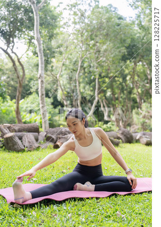 Yoga flexibility. Young woman reaching for her foot on yoga mat outdoors. 128225717