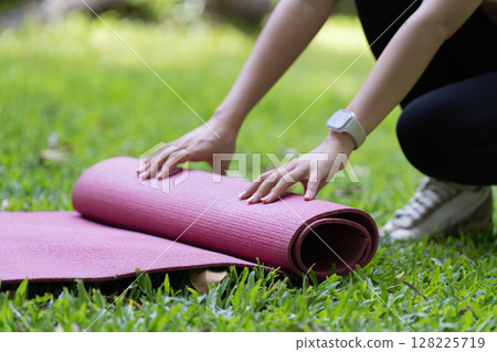 Yoga mat preparation. Close-up of hands rolling yoga mat on grass. 128225719