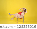 Cheerful Woman Relaxing on a Chair Against Vibrant Yellow Background 128226016