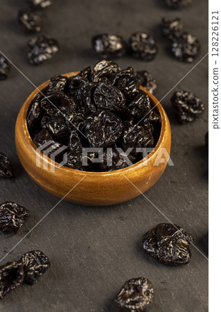 bowl filled with dried prunes closeup, dark dried plum fruits poured into a bowl 128226121