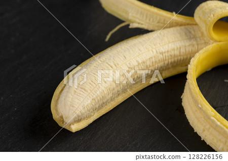 open ripe yellow banana on a black slate board, ripe and sweet yellow banana on a kitchen board made of black stone open ripe yellow banana on a black slate board, ripe and sweet yellow banana on a kitchen board made of black stone 128226156