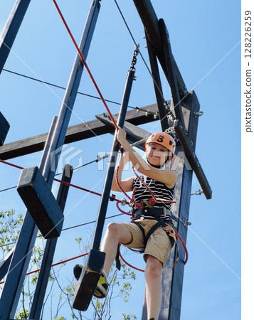 a brave boy in outdoor rope park passing obstacle course. Active summer holidays a brave boy in outdoor rope park passing obstacle course. Active summer holidays 128226259