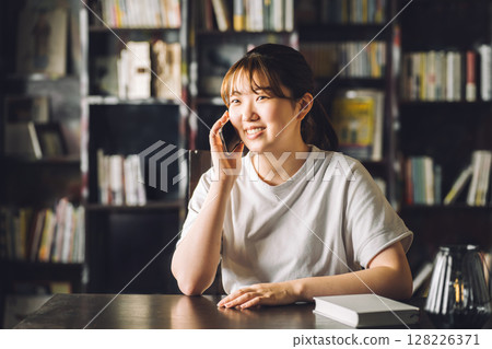一名女大學生在書房或圖書館打電話 128226371