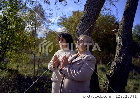 middle-aged woman and elderly mother with holy bible in hands praying for peace in autumn forest middle-aged woman and elderly mother with holy bible in hands praying for peace in autumn forest 128226381