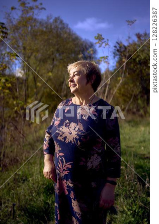 a   portrait of an elderly woman with gray hair in a dress  in the autumn forest 128226387
