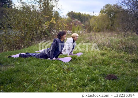 middle-aged woman teaches her old mother somatic exercises and yoga to maintain health by the river in autumn middle-aged woman teaches her old mother somatic exercises and yoga to maintain health by the river in autumn 128226394