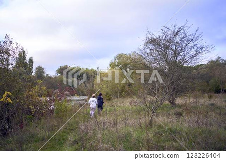 A middle-aged woman and her old mother take a morning jog together to maintain health by the river in autumn 128226404