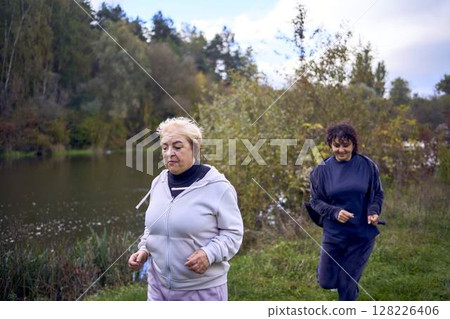 A middle-aged woman and her old mother take a morning jog together to maintain health by the river in autumn A middle-aged woman and her old mother take a morning jog together to maintain health by the river in autumn 128226406
