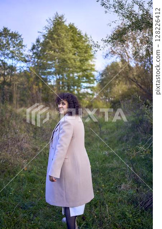 middle-aged woman with dark curly hair in light beige suit and coat enjoying nature in autumn forest middle-aged woman with dark curly hair in light beige suit and coat enjoying nature in autumn forest 128226412
