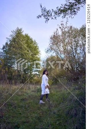 middle-aged woman with dark curly hair in light beige suit enjoying nature in autumn forest 128226414