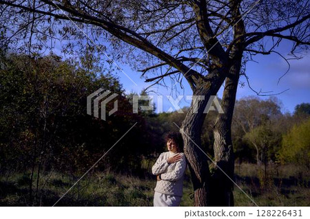 middle-aged woman with dark curly hair in light beige suit enjoying nature in autumn forest middle-aged woman with dark curly hair in light beige suit enjoying nature in autumn forest 128226431