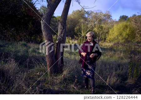 portrait of an elderly woman with gray hair in a dress and shawl in the autumn forest 128226444