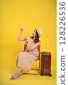 Traveler Sitting on a Chair with Luggage Against a Yellow Background 128226536
