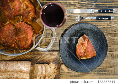 Juicy roasted meat dish served with fresh bread and red wine on rustic wooden table 128227245
