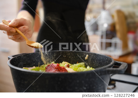 A person is adding spices to a pot filled with chopped vegetables and meat A person is adding spices to a pot filled with chopped vegetables and meat 128227246