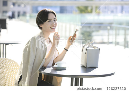 一位神態放鬆的女士在咖啡館露臺上看著她的智慧型手機。 128227810