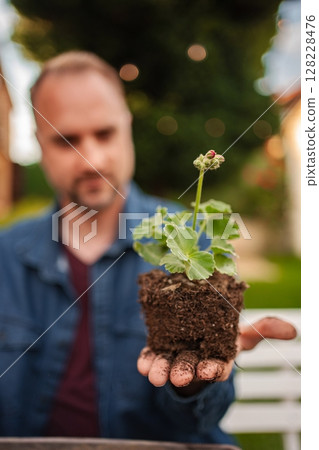 Man holding potted plant with soil in garden setting 128228476
