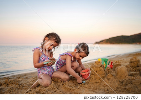Siblings building sandcastles at sunset on a tranquil beach 128228700
