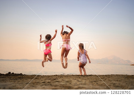 Joyful sisters jumping on the beach at sunset by the water 128228701