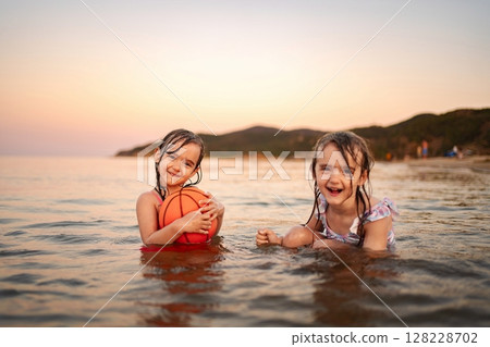 Joyful sisters playing in the water at the beach during sunset 128228702